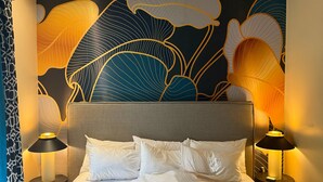 A hotel room with a large bed, two bedside tables with lamps, and a wall with a large floral pattern.