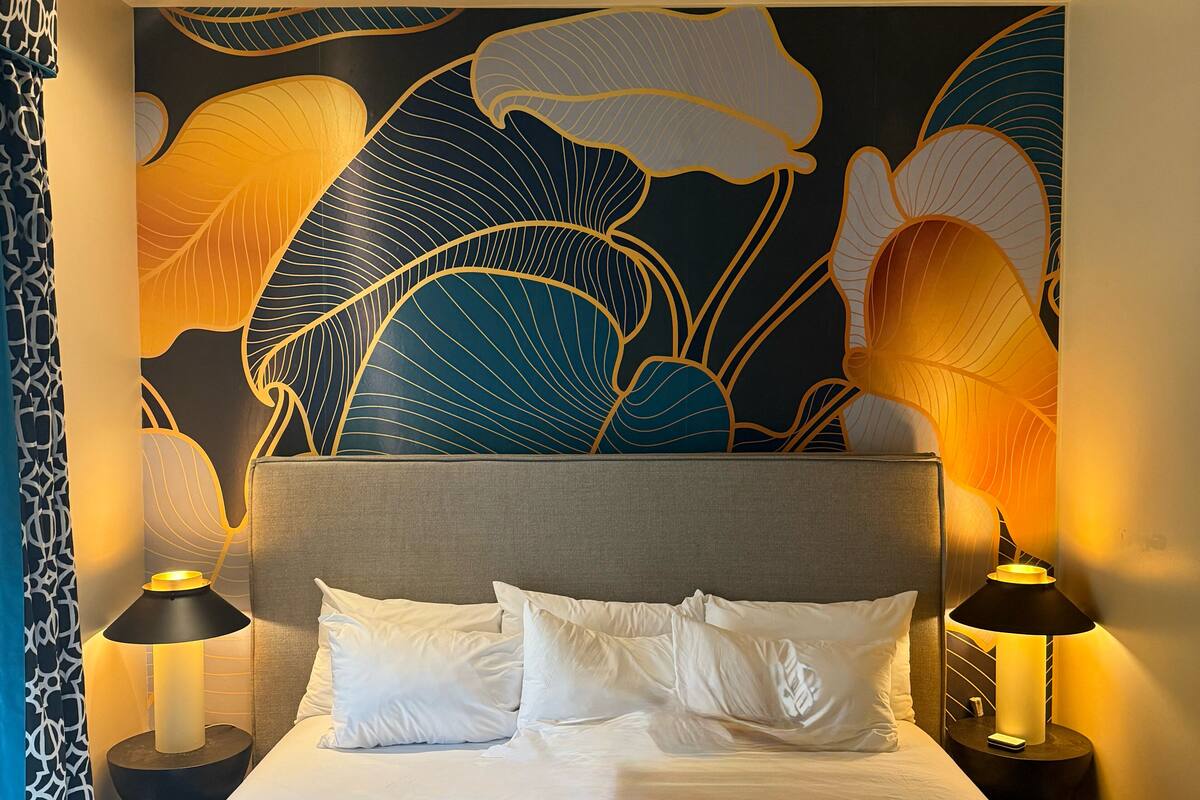 A hotel room with a large bed, two bedside tables with lamps, and a wall with a large floral pattern.
