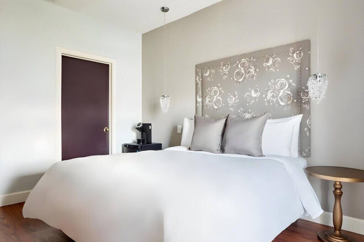 A hotel room with a large bed, a bedside table with a lamp, a decorative headboard, and a door.