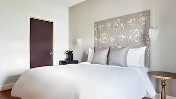 A hotel room with a large bed, a bedside table with a lamp, a decorative headboard, and a door.