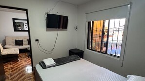 Een slaapkamer met een bed, een aan de muur bevestigde televisie, een raam met uitzicht en een deur die naar een andere kamer leidt.