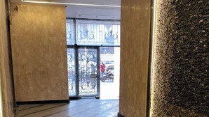 Um corredor com piso de mármore, parede texturizada e vista para o exterior através de uma porta de vidro.