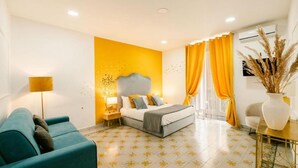 Ein modernes Hotelzimmer mit Bett, Sofa, Nachttisch, Lampe und einer Vase mit Trockenpflanzen.