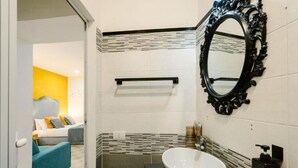 Ein Badezimmer mit weißem Waschbecken, schwarzem Spiegel und gefliesten Wänden.