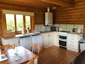 Eine kompakte Küche mit Mikrowelle, Herd und Spüle, Holzschränken und einem Esstisch mit Stühlen.