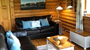 Et interiør af en træhytte med en sort lædersofa, et træbord og et maleri på væggen.