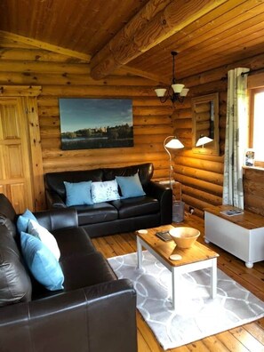 Ein Interieur einer Blockhütte mit einem schwarzen Ledersofa, einem Holztisch und einem Gemälde an der Wand.