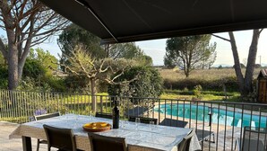 An outdoor patio with a table and chairs, a pool, and a view of trees and hills.