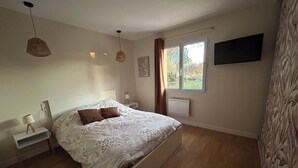 A bedroom with a bed, bedside tables, a window, a radiator, and a wall-mounted TV.