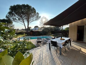 An outdoor patio with a pool, a table set for dining, and a covered seating area.