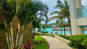 A pathway leading to a pool area with palm trees and a modern building. - Apartment with balcony overlooking crystal-clear lagoon and (Mazatlán)