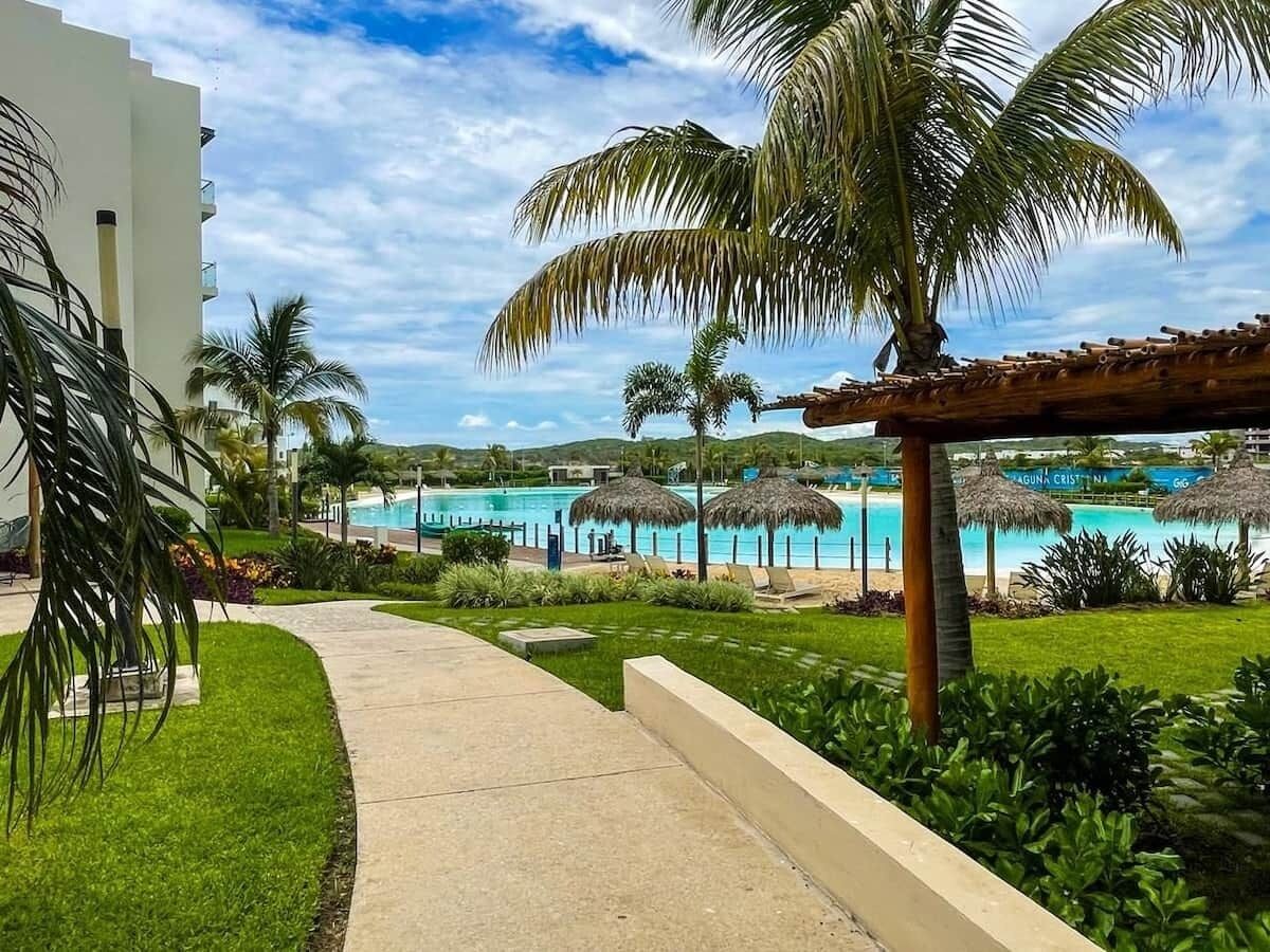 Een resort met een zwembad, palmbomen en rieten parasols.