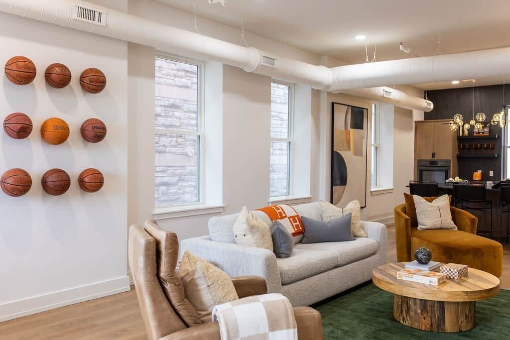 A living room with a sofa, armchairs, a coffee table, and a wall with basketballs.