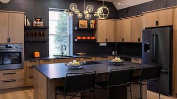 A modern kitchen with wooden cabinets, a black refrigerator, and a central island with chairs.