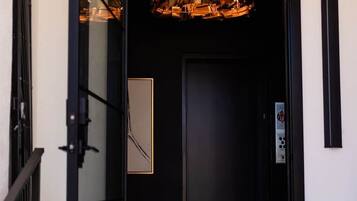 A modern elevator with a glass door, a metal handrail, and a decorative light fixture above the door.