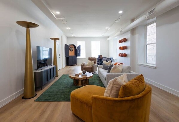 Un salon moderne avec un canapé, un fauteuil et une table basse. On y trouve également une télévision, une cheminée et une fenêtre avec des rideaux.