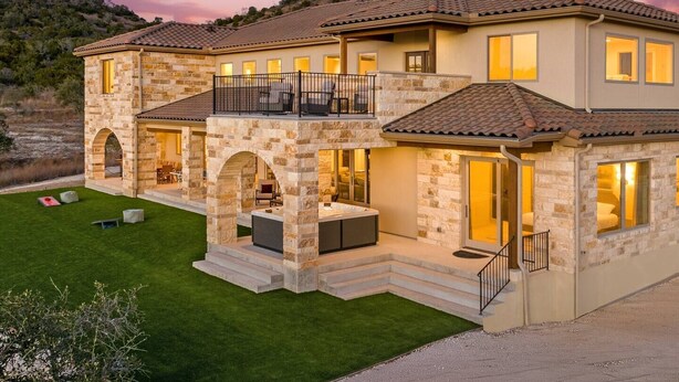 A two-story house with a stone facade, a balcony, and a well-maintained lawn.