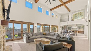 A spacious living area with a large sectional sofa, a coffee table, and a fireplace. There are multiple windows providing natural light and views of the outdoors.