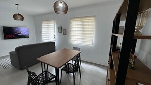 A modern living room with a wooden dining table, black chairs, a grey sofa, and a TV on the wall. - 3-BEDROOM APARTMENT WITH POOL AND GARAGE | CRISTO REI (Teresina)