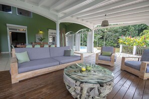 A covered outdoor seating area with a sofa, chairs, and a glass-top coffee table. - Large 5-bedroom villa with pool in the heart of the island (Petit-Bourg)
