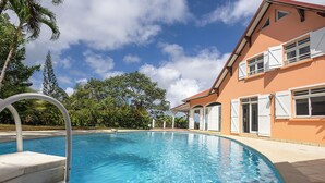 Una piscina con superficie d'acqua cristallina e azzurra, circondata da un edificio con persiane bianche e tetto rosso.