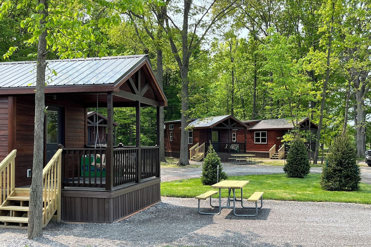 A cabin-style lodging with a porch, picnic table, and a gravel driveway.