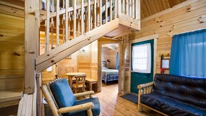 Interno di una baita in legno con una scala, un divano, un tavolo da pranzo e un letto.