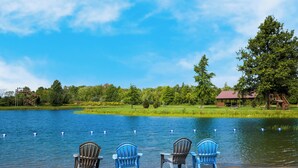 Tre poltrone Adirondack vicino a un lago, con un pontile di legno e un gazebo sullo sfondo.