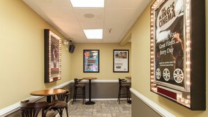 Un cine con un cartel que anuncia películas excelentes a diario, una pequeña zona de bar con taburetes y un suelo de baldosas.