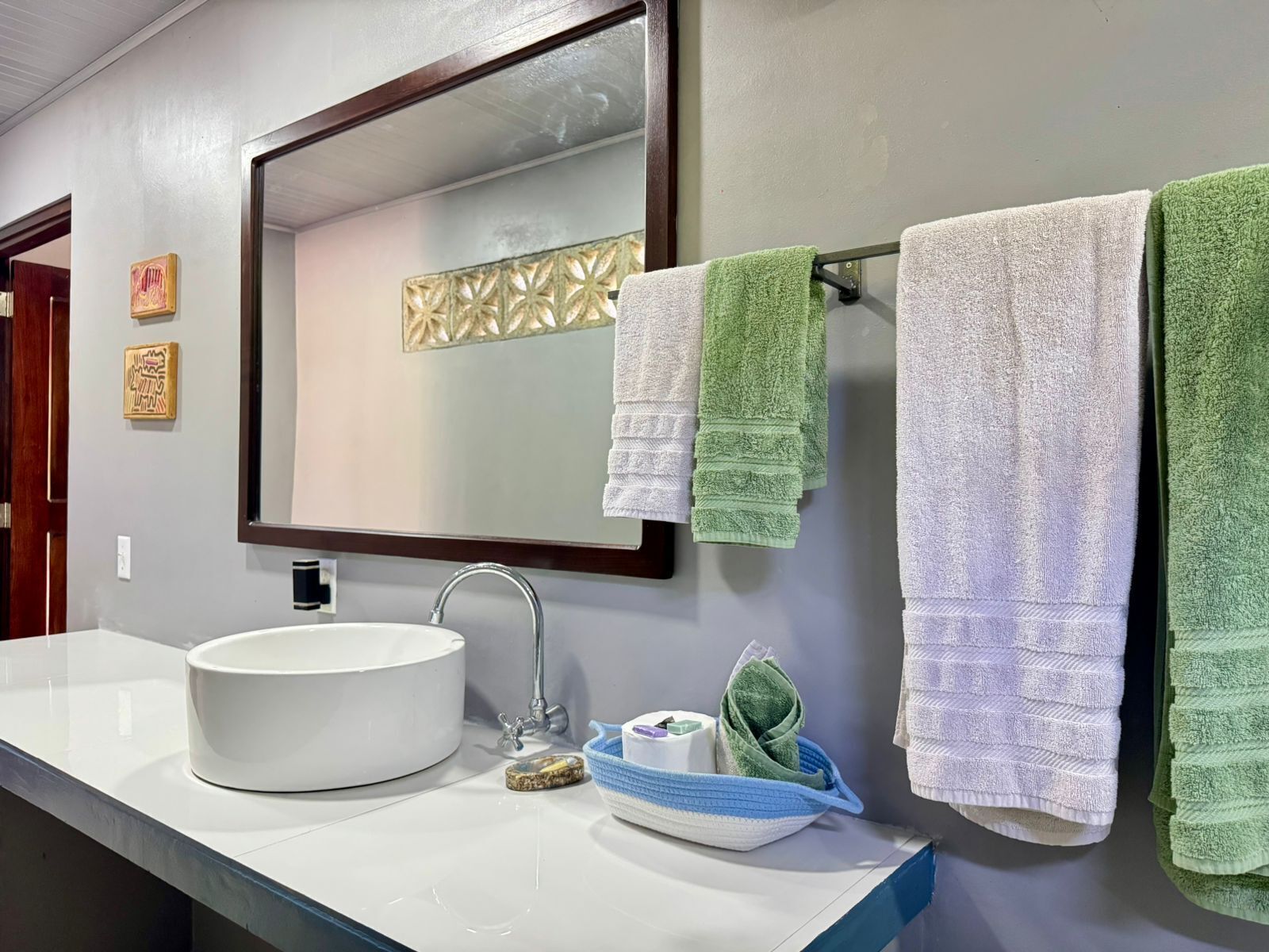 Une salle de bain avec un lavabo blanc, un miroir et trois serviettes suspendues à un porte-serviettes.