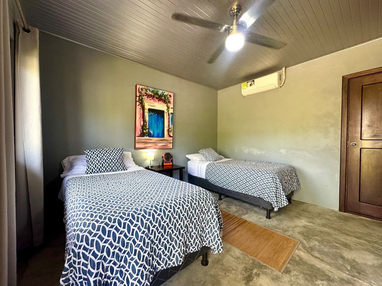 A hotel room with two beds, a ceiling fan, an air conditioning unit, and a door.
