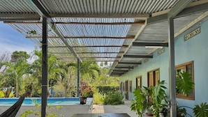 Uma área externa coberta com piscina, plantas em vasos e uma mesa.