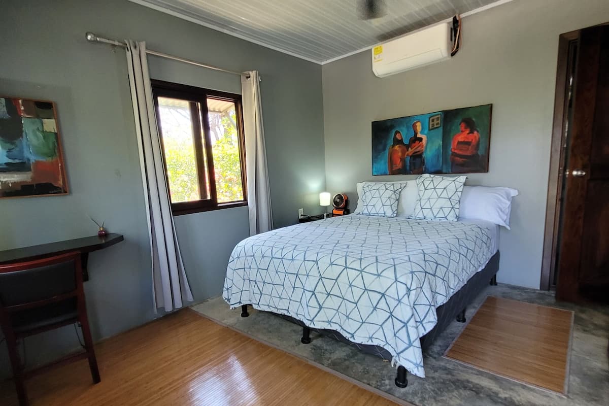 A bedroom with a bed, a desk, a chair, a ceiling fan, and a window with curtains.