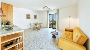 A modern living room with a sofa, a dining table with chairs, a kitchen area with a sink and cabinets, and a large window providing a view of the outdoors. - Casa Luisa Boutique Stay with Vegetable Garden and Sea View (Forio)