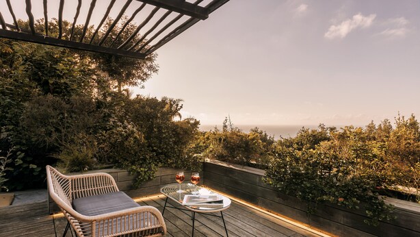 A wooden deck with wicker chairs and a glass table, overlooking a lush garden and a distant view. - Casa Luisa Boutique Stay with Vegetable Garden and Sea View (Forio)