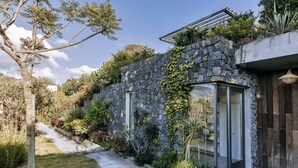 A stone building with a glass door, surrounded by lush greenery and a stone pathway. - Casa Luisa Boutique Stay with Vegetable Garden and Sea View (Forio)