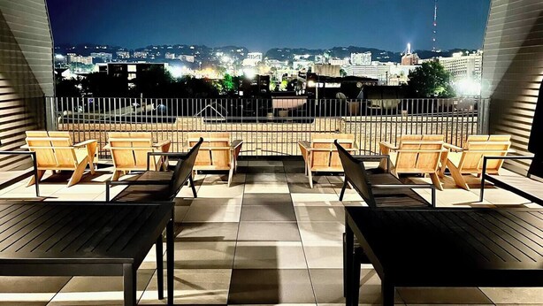 A rooftop terrace with wooden chairs and tables, offering a view of a cityscape at night. - Cobblestone Chic - WiFi/Downtown/Walk Score 91 (Birmingham)