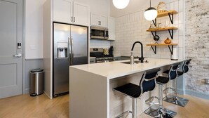 A modern kitchen with a central island, stainless steel appliances, and a brick accent wall. - Cobblestone Chic - WiFi/Downtown/Walk Score 91 (Birmingham)