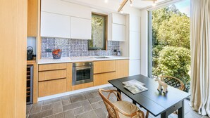 A modern kitchen with wooden cabinets, a built-in oven, and a large window overlooking a garden.