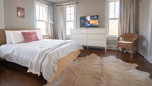 Ein Schlafzimmer mit einem Bett, einem Fernseher, einem Schminktisch, einem Sessel und einem Teppich.