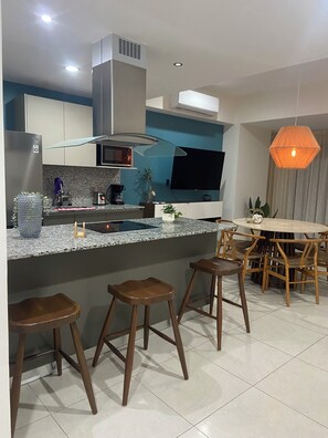 A modern kitchen with a central island, bar stools, a dining table with chairs, and a pendant light. - Spectacular ocean view (Mazatlán)