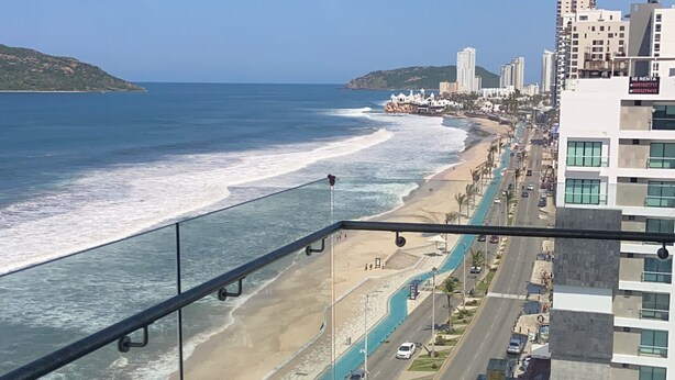 A balcony with a view of a beach and ocean, a road with cars, and buildings in the background. - Spectacular ocean view (Mazatlán)