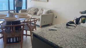 A modern kitchen with a granite countertop, a dining area with wicker chairs, a white sofa, and a large window overlooking the sea. - Spectacular ocean view (Mazatlán)