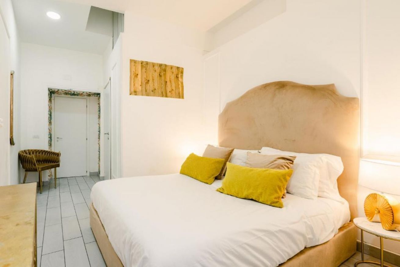 A bedroom with a large bed, a bedside table, a chair, and a wooden artwork on the wall.