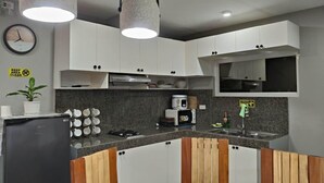 Cocina moderna con armarios blancos, un refrigerador negro, un microondas y un lavamanos. Hay dos lámparas colgantes, un reloj y un letrero que dice 'Mantener el área limpia'.