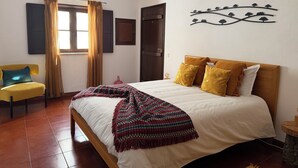 Un dormitorio con cama, una silla, un ventanal con cortinas y un adorno en la pared.