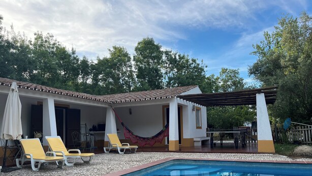 Una piscina con plataforma de baldosas, sillas de descanso amarillas y un área de patio cubierta con una hamaca.