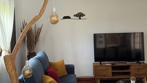 Una sala de estar con un sofá azul, un mueble de televisión de madera, un televisor de pantalla plana y dos lámparas colgantes.