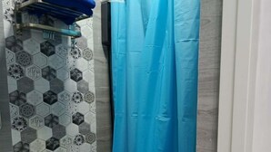 A bathroom with a toilet, a shelf with a blue towel, a shower curtain, and a wall with hexagonal patterned tiles. - Cozy Escape with WiFi & Smart TV (Dipolog City)