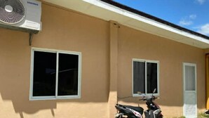 A building with a Samsung air conditioning unit, two windows, and a parked motorcycle. - Cozy Escape with WiFi & Smart TV (Dipolog City)